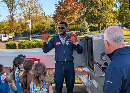 A Suburban Propane driver stand at the back of a propane bobtail and speaks to a Girl Scout troop and their moms about driving at the Trucks Are for Girls event