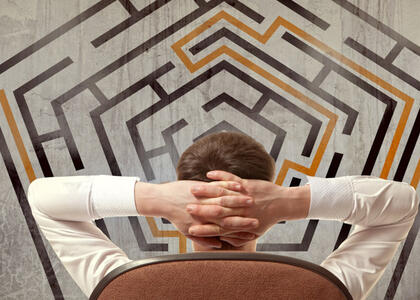 A man stands with hands folded behind his head looking a 2D maze, showing ins and outs of exit planning.