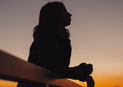 A woman's silhouette peers off into the night sky at dusk, reflecting this month's Verbatim question.